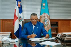 Venancio Alcántara signing documents in his office, behind shutters and flags.
