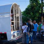 Agentes de la DGM en camión de control migratorio con la puerta abierta y reviendo una extranjera, alrededor personas observando.