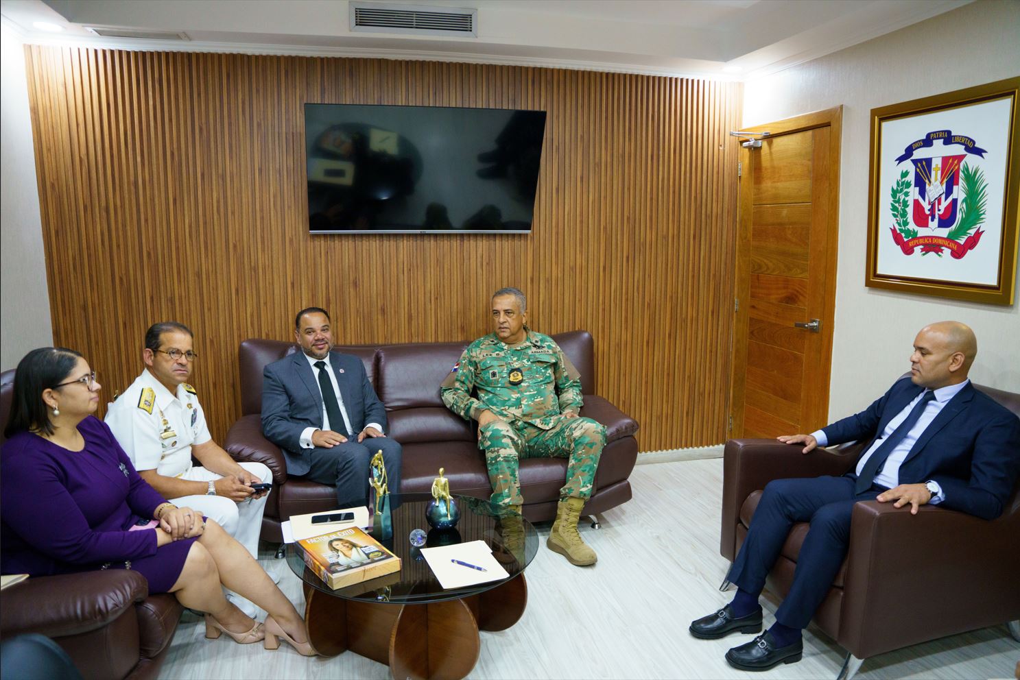 Director General in camouflage uniform, together with the Ombudsman, officials and a Navy officer, gathered in the office with the national coat of arms and a screen in the background.