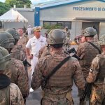 A group of Dominican military personnel in camouflage uniform and helmet receive instructions from the Director General in front of the Haina Data Processing building.