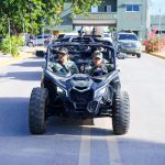 Director General together with other officers in camouflage uniform in a military raptor buggy in front of Fortaleza Enriquillo, with vehicles and people in the background.