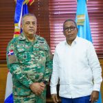 General manager with economic dining director in office pose in front of flags and a backdrop of wooden shutters.