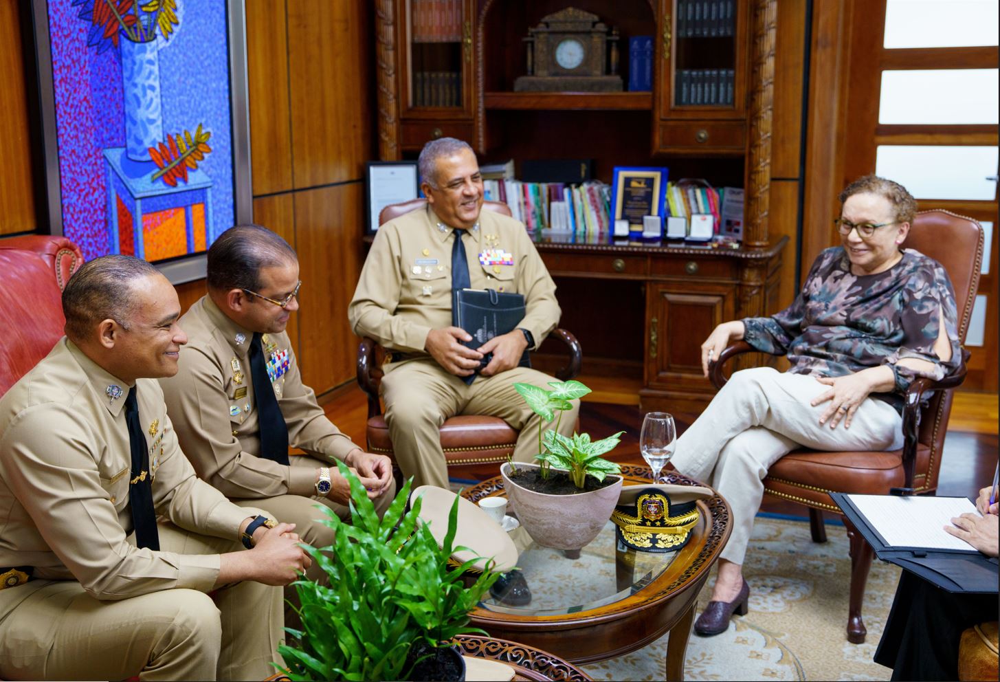 Meeting of the Director General with the Attorney General of the Dominican Republic with other departmental directors of the DGM seated around a table decorated with plants, books and a military cap.