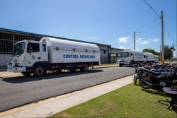 White trucks from the Directorate General of Migration, identified as "Immigration Control", parked in front of a building under a clear sky, with motorcycles parked on the right side.