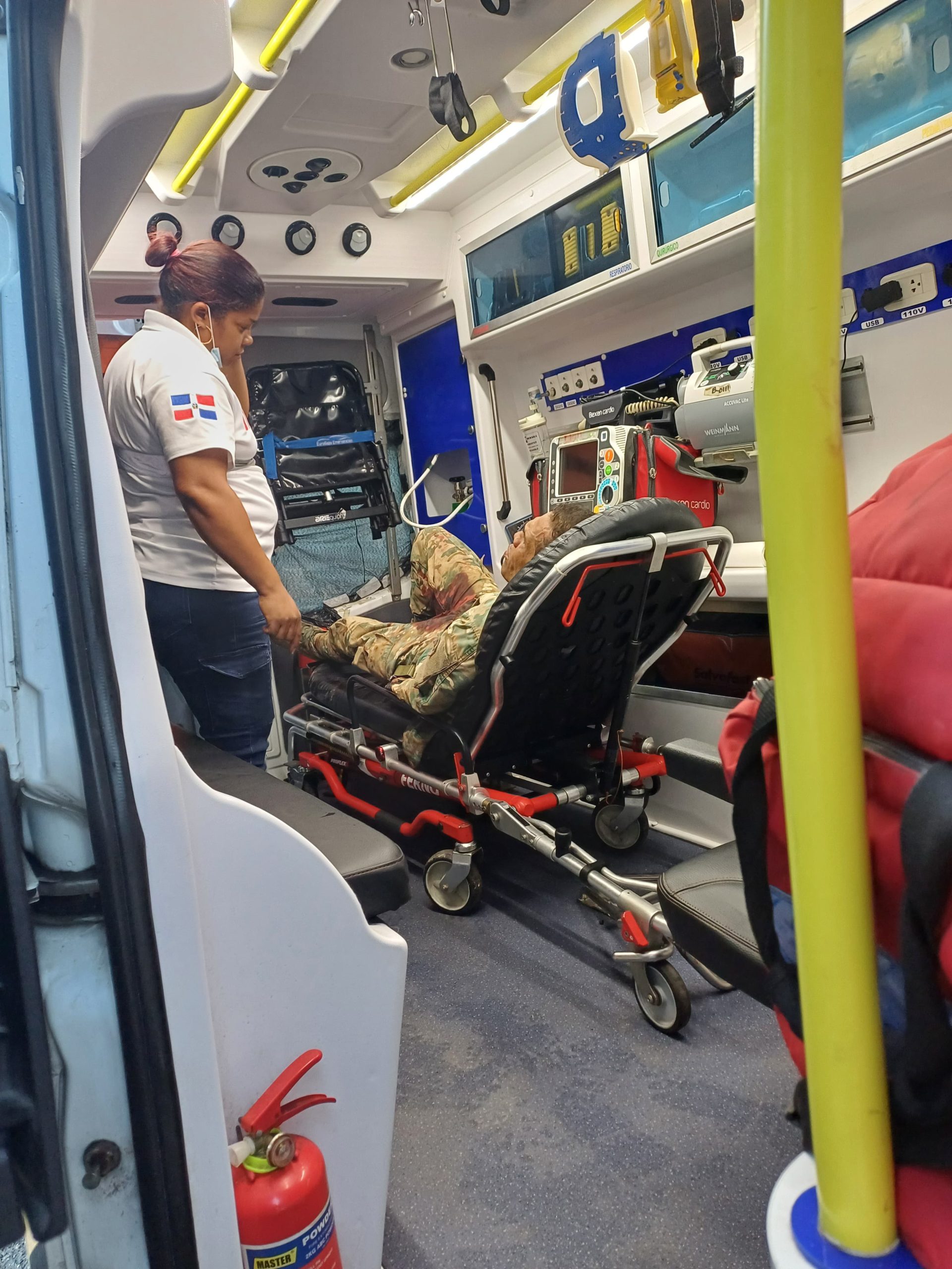 Soldier wounded by bullet in ambulance, lying on a stretcher with a nurse next to him.