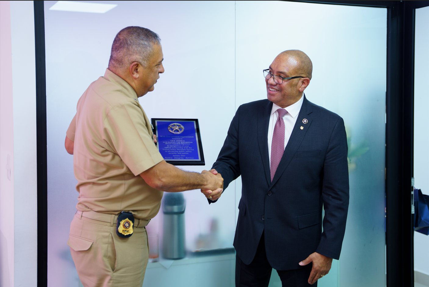 Director de Migración saludando con un estrecho de mano al director del Servicio de Marshals de Estados Unidos (USMS) y recibiendo un reconocimiento por su colaboración.