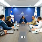 Director General of the DGM with the Minister of Public Health sitting at a meeting table in front of the Dominican flag and the public health flag in the office of Victor Atallah. The Minister of Health, among other authorities present.