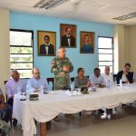 Director General, with provincial authorities sitting at a table and the Director General of Migration standing and talking.