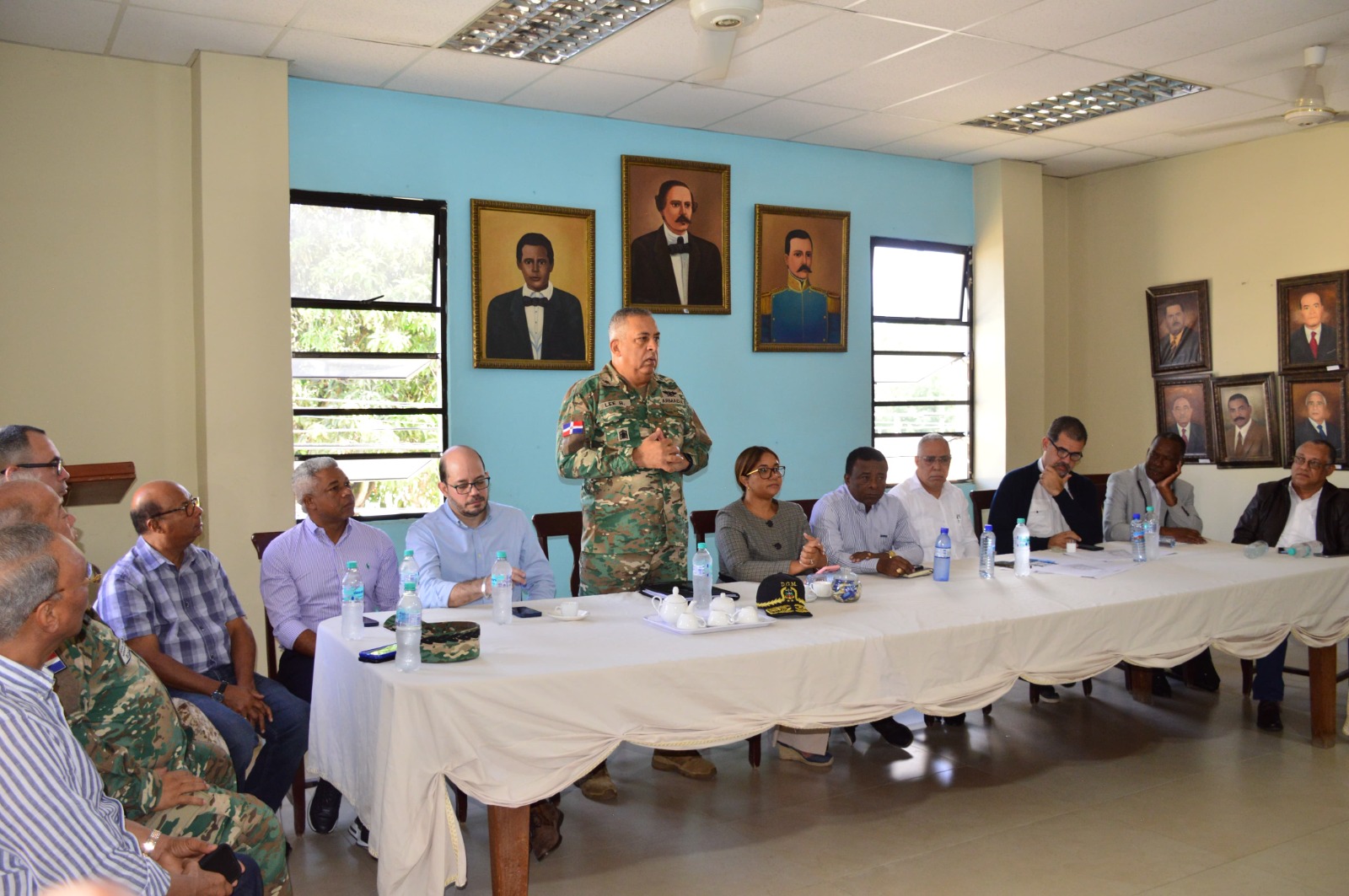 Director General, with provincial authorities sitting at a table and the Director General of Migration standing and talking.