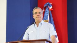 Photo of President Luis Abinader standing at a brown podium in front of the Dominican flag.