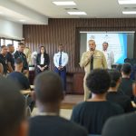 Director DGM dando bienvenida a nueva unidad de reacción rápida en salón de UNICARIBE, unidad sentada y autoridades DGM parados.