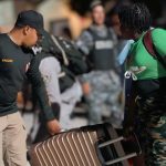Immigration agent helping an undocumented foreigner carrying a suitcase.