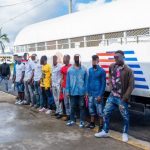 Extranjeros irregulares detenidos, todos parados frente a camión control migratorio.